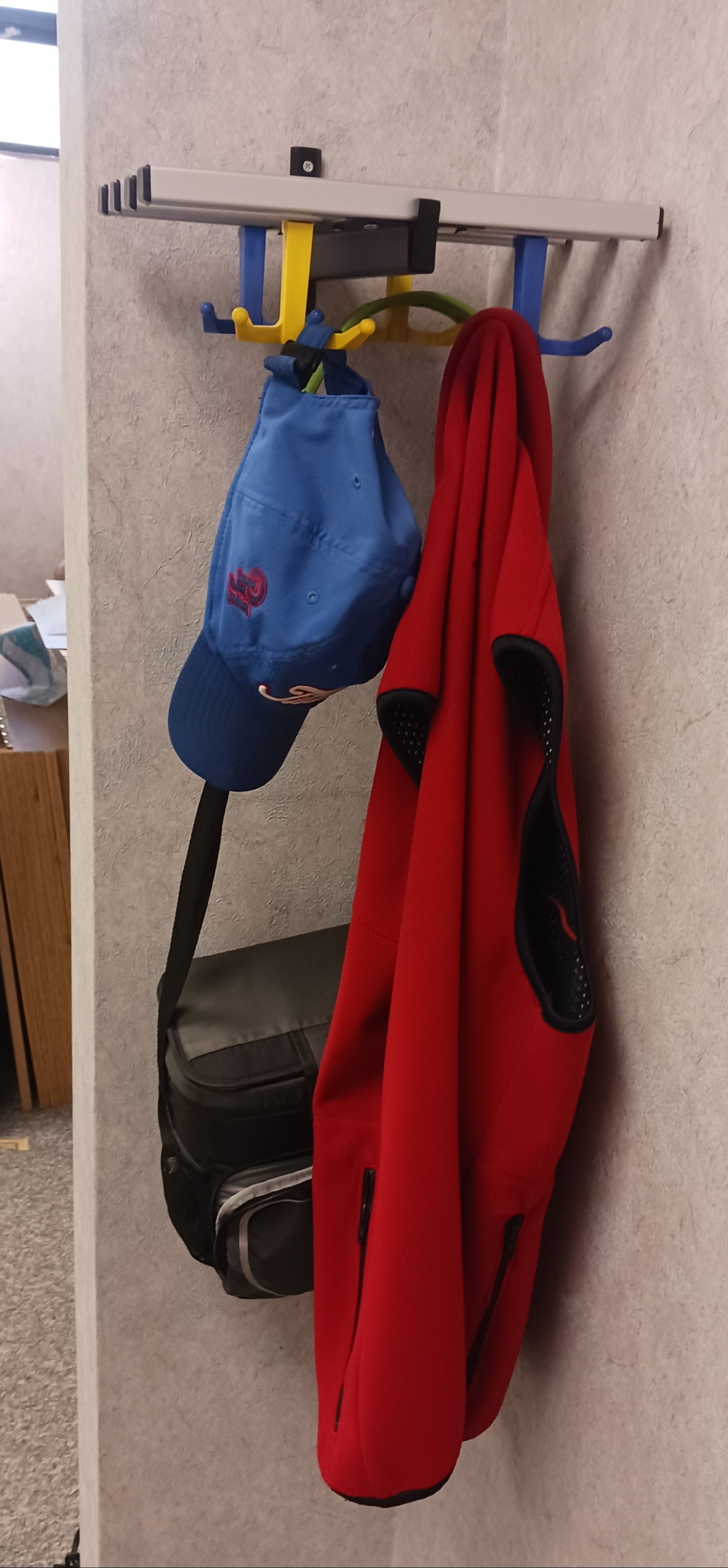Red jacket, blue cap, and black bag hanging on a wall-mounted coat rack.